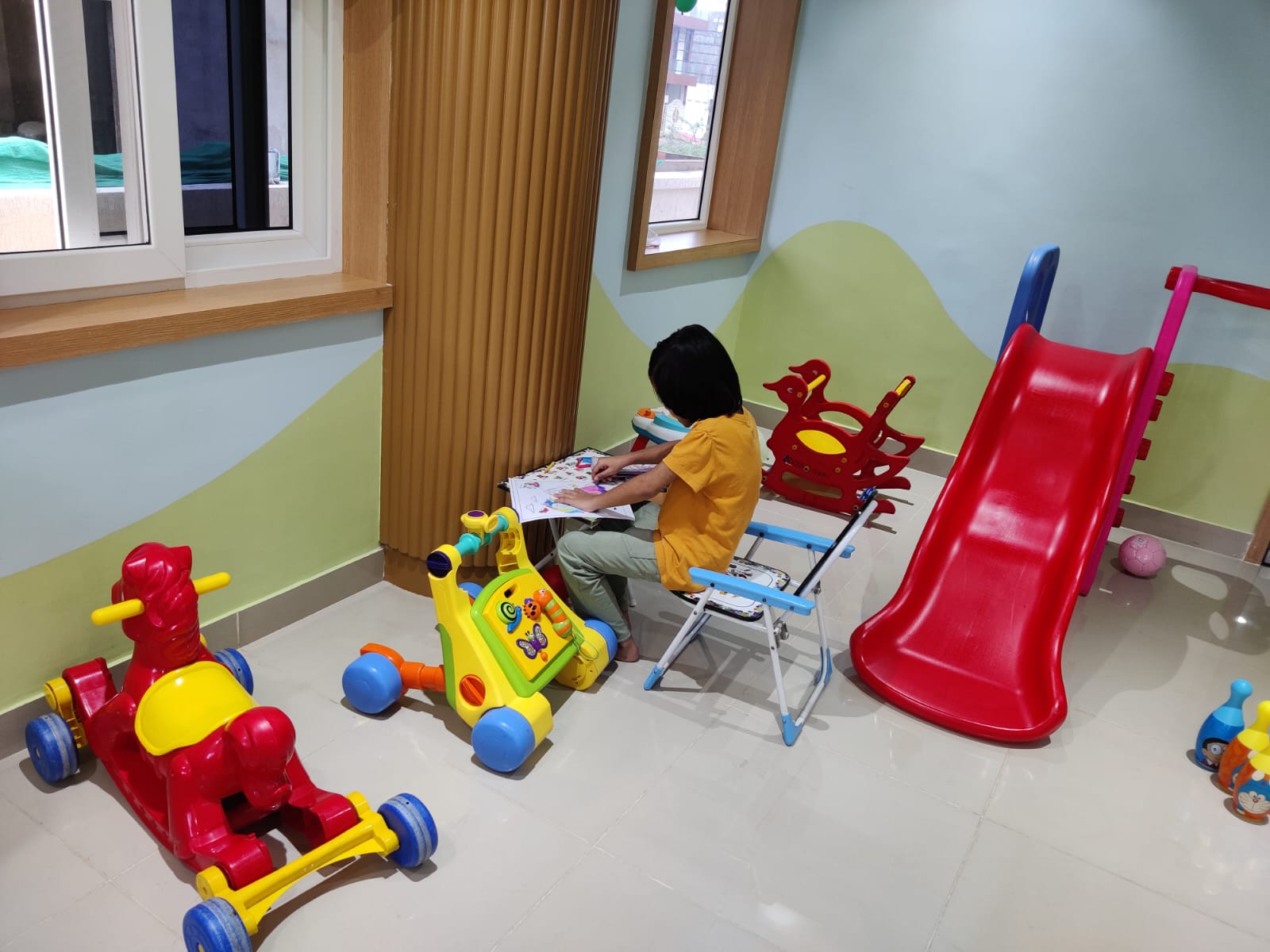 Child playing with colorful toys beside a slide in the pediatric waiting area